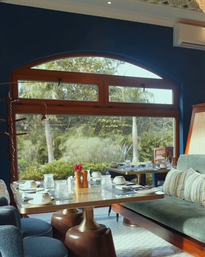 Breakfast tables set by a tall arched window in the hotel's blue dining room, with velvet chairs and banquette