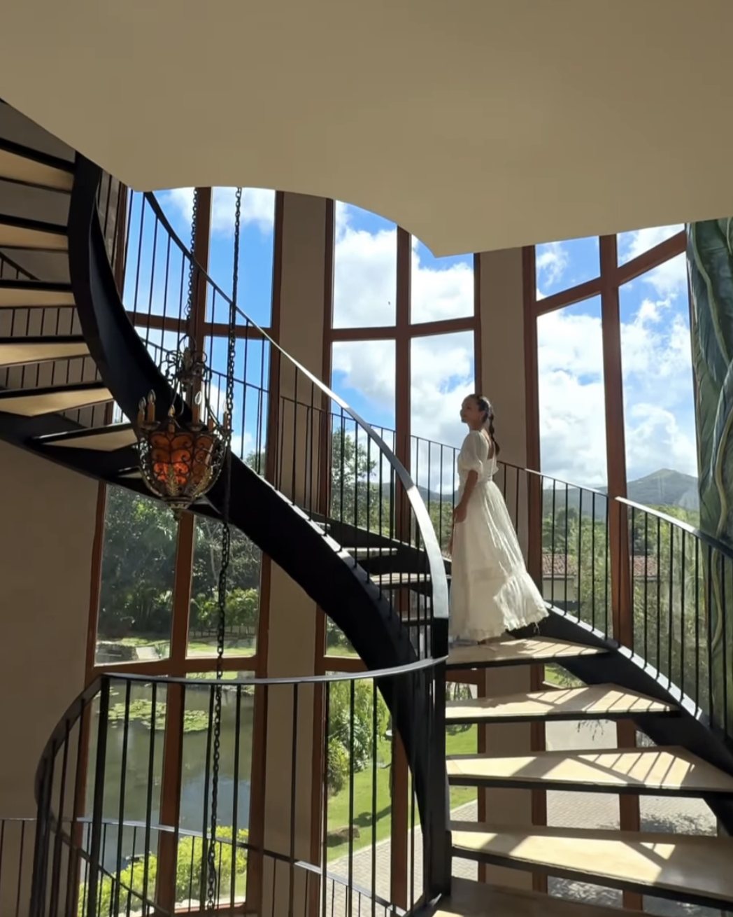 A woman in a white dress on the spiral staircase in the hotel's glass tower, the gardens and mountains beyond